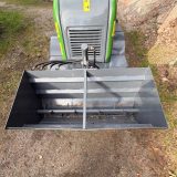 Sandspridare för lastmaskin sedd uppifrån – sandlåda med matarvals och hydraulslangar